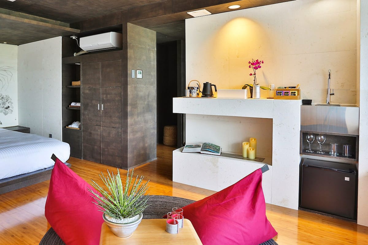 A modern bedroom with a large bed, a small desk, and a kitchenette.
