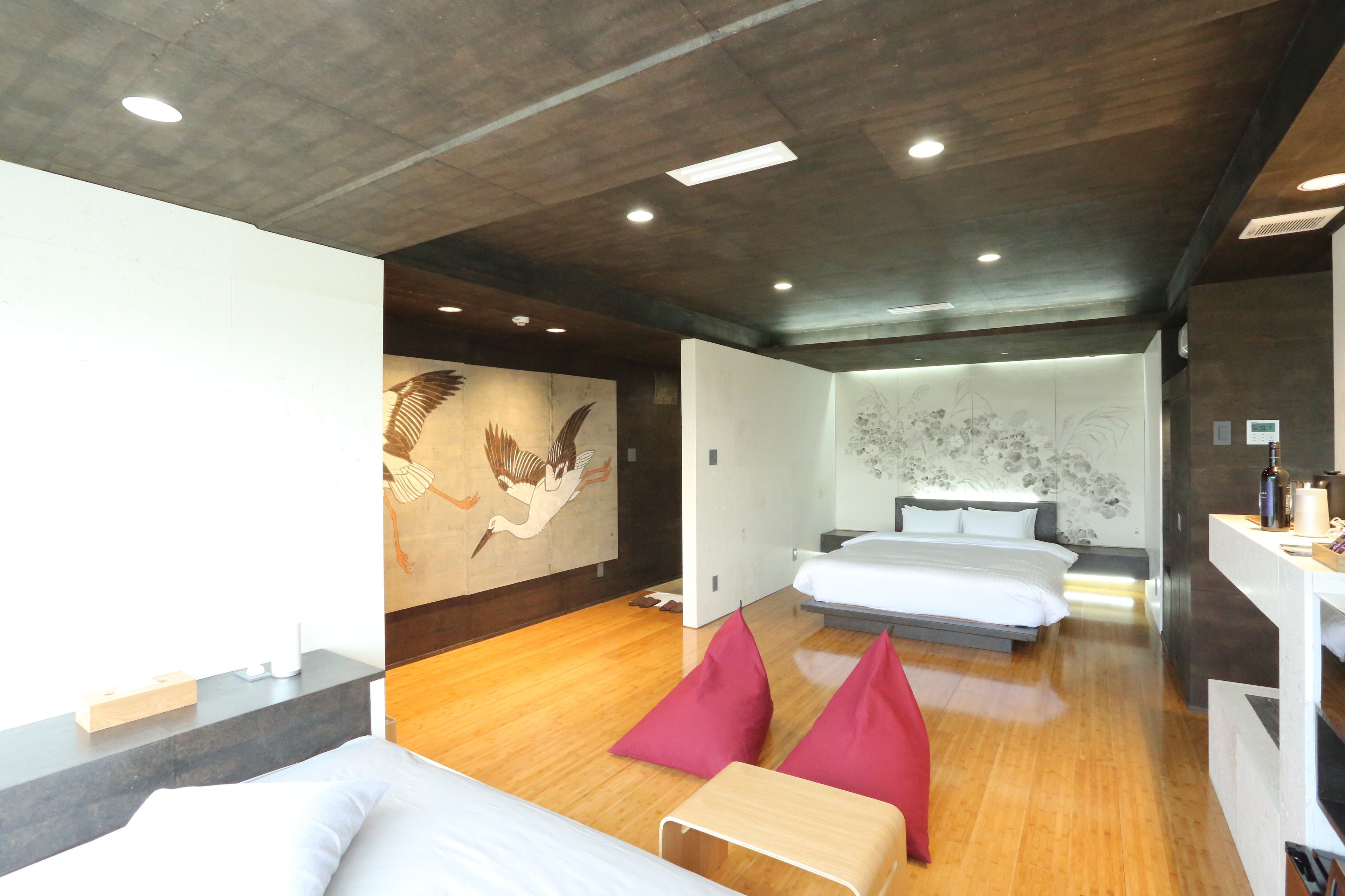 Una habitación de hotel con piso de madera, una cama, un escritorio con computadora y una pared decorada con un mural.