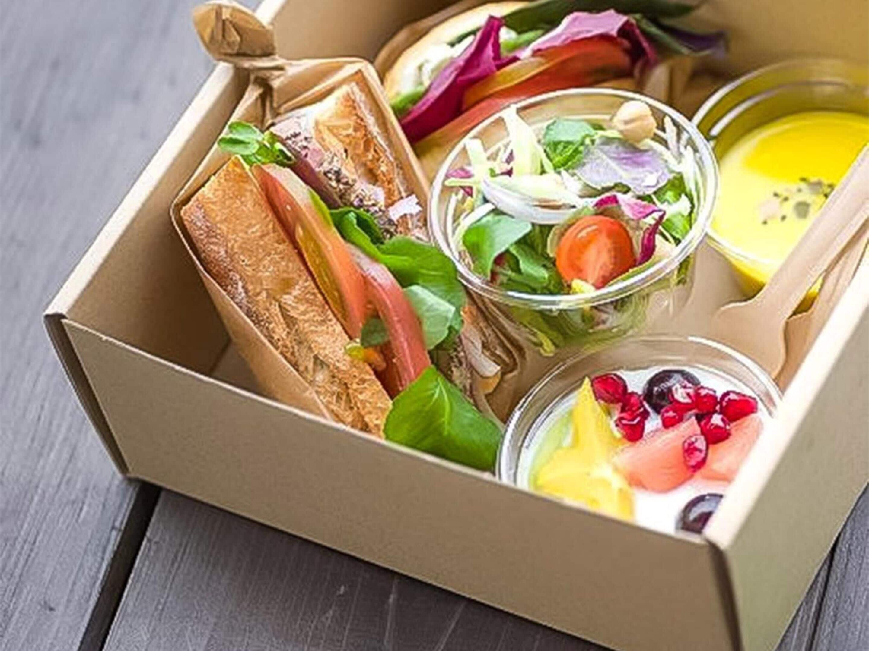 A lunch box containing sandwiches, a salad, and two small bowls with fruit and soup.