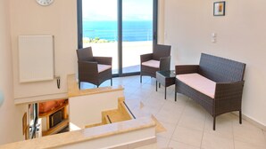 Un salon comprenant un canapé, deux fauteuils, une table basse et une vue sur l’océan, accessible par une porte-fenêtre coulissante.