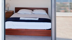 Une chambre à coucher comprenant un lit, une table de chevet, une lampe et une vue sur l’extérieur grâce à une grande fenêtre.