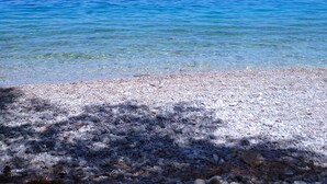 Une plage de galets bordée d’une eau d’un bleu limpide et donnant sur une terre lointaine.