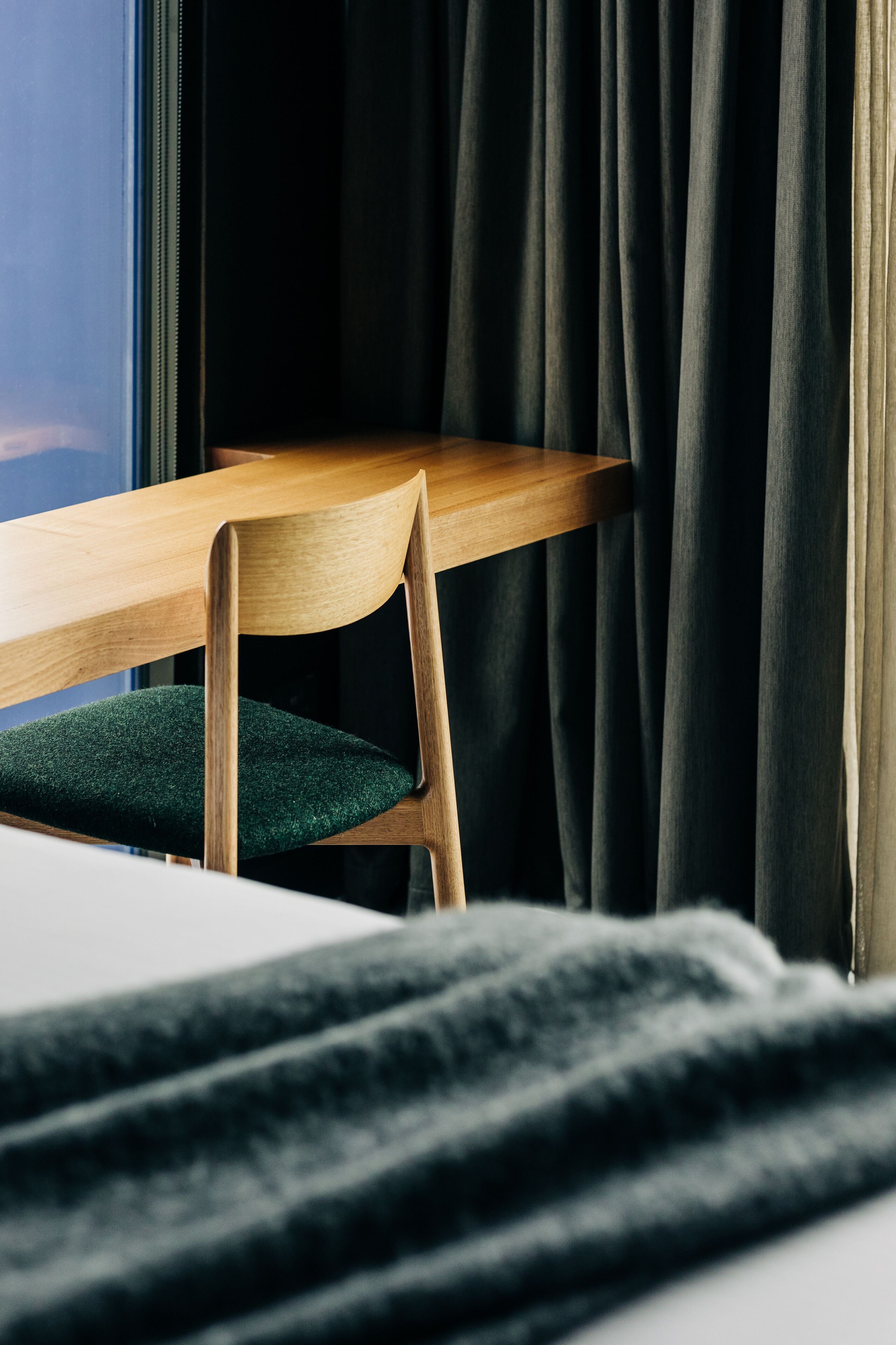A wooden chair with a green cushion in a room with a window and dark curtains.