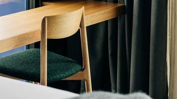 A wooden chair with a green cushion in a room with a window and dark curtains.