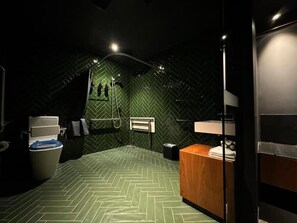 A small, dimly lit room with a herringbone-patterned floor, a toilet, a sink, and a shower area. - Moss Hotel (Battery Point)