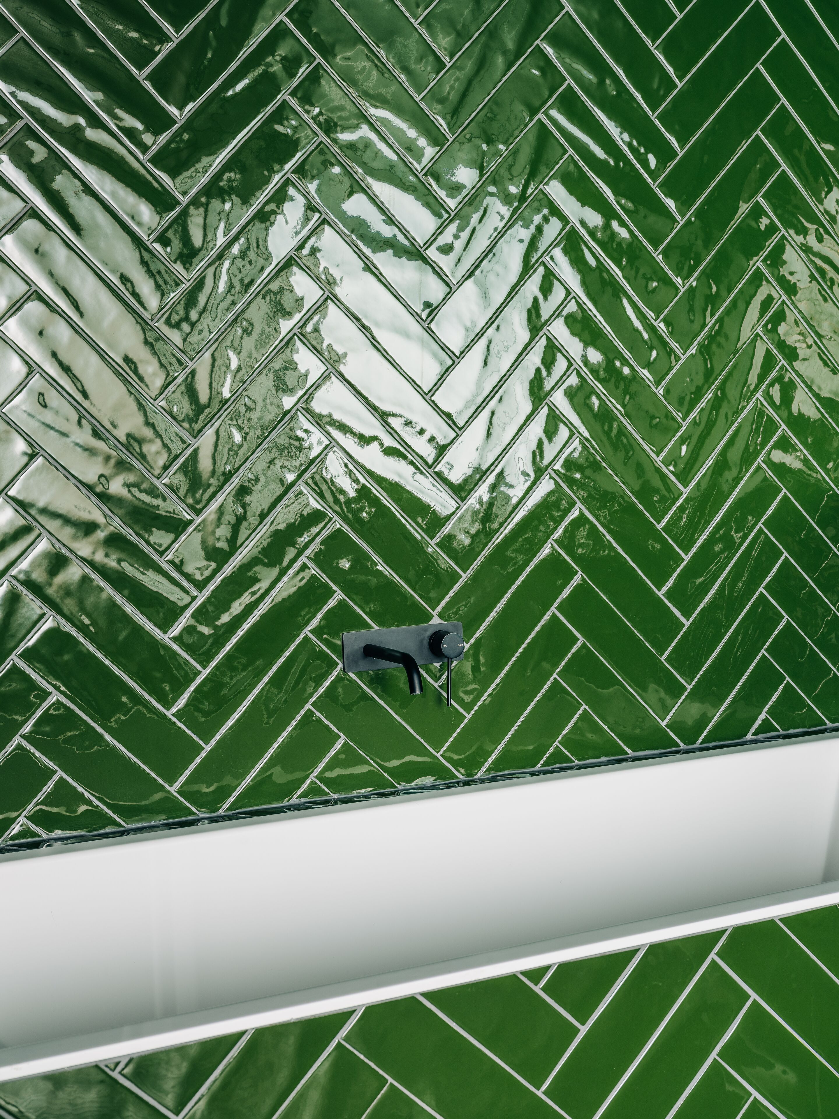 Une salle de bain avec un carrelage vert disposé en motif chevrons et un robinet noir.