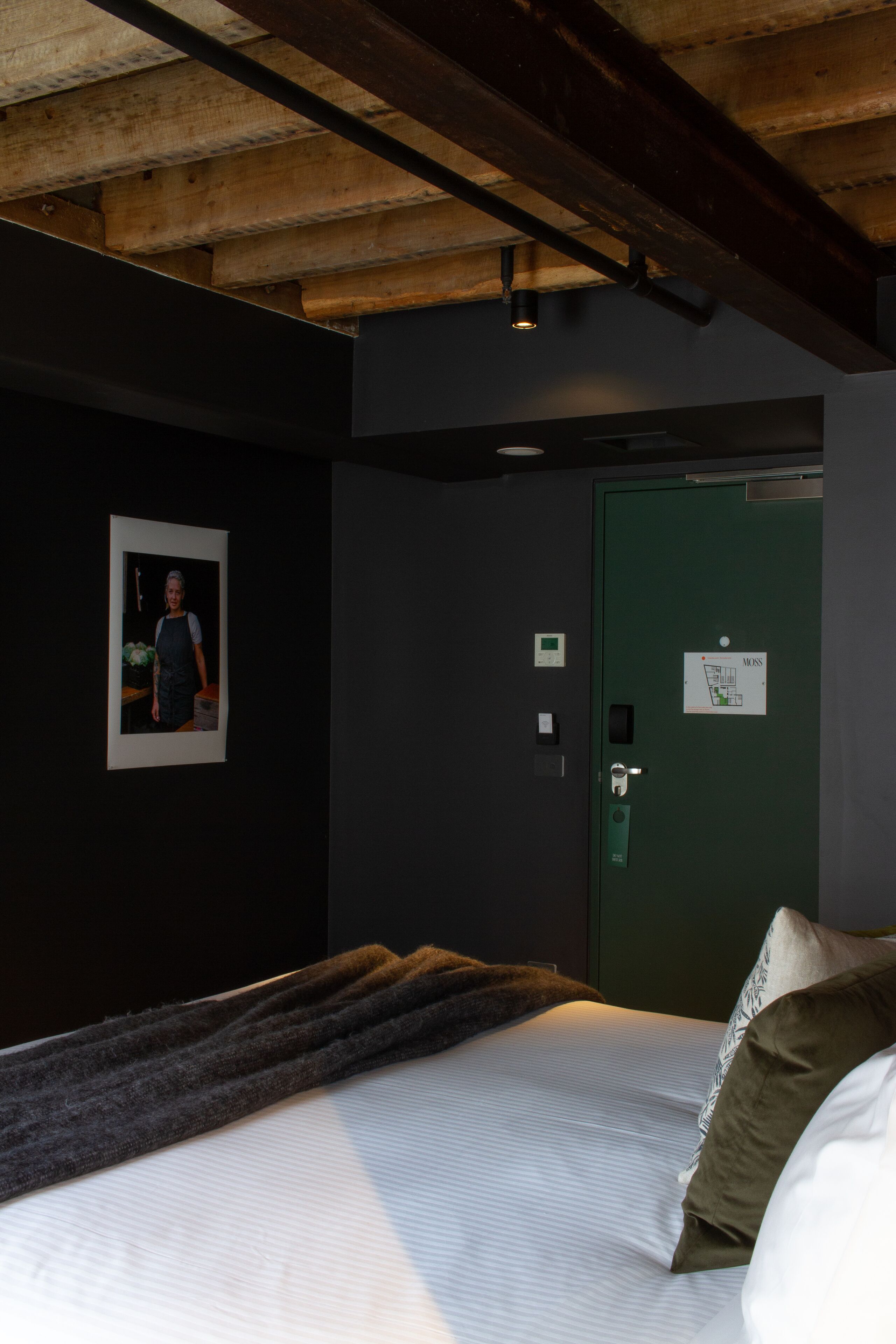 A bedroom with a bed, a green door, and a framed picture on the wall.