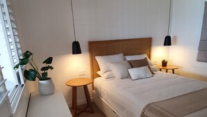 A bedroom with a bed, bedside tables, a small round table, a potted plant, and a ceiling fan. - Saltwater Apartments (Lake Cathie)
