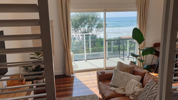 A cozy living room with a leather sofa, a coffee table, and a view of the ocean through large glass doors. - Saltwater Apartments (Lake Cathie)