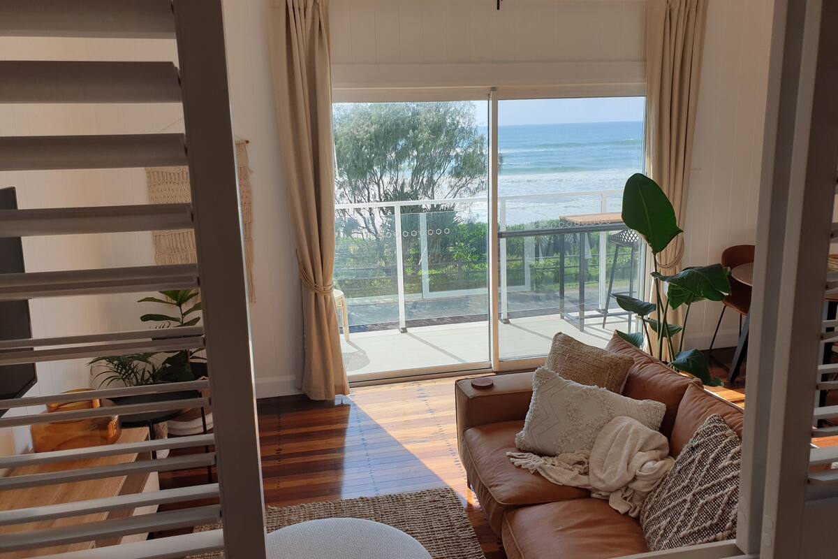 A cozy living room with a leather sofa, a coffee table, and a view of the ocean through large glass doors.