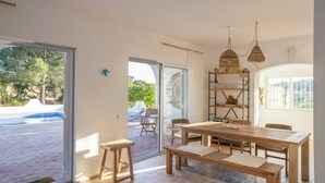 A dining area with a wooden table and benches, a glass door leading outside, and a shelf with glassware. - Casa La Paz, trendy home of peace. (Faro)