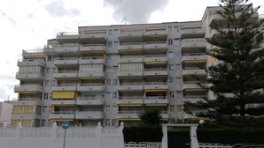Un edificio residencial de varios pisos con balcones, un acceso con portón y una calle delante.