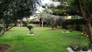Un jardín bien cuidado con diversas plantas y árboles, un cielo despejado y una valla al fondo.