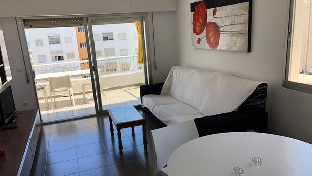 Un salón moderno con un sofá blanco, una mesita redonda y un ventanal con vistas a un edificio y un balcón.