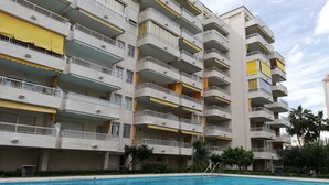 Un edificio residencial de varios pisos con balcones, piscina y follaje circundante.