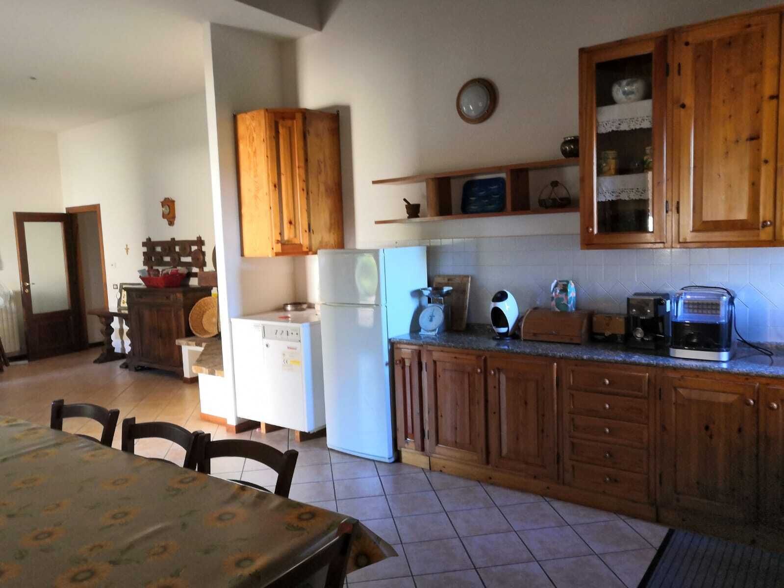 A kitchen with wooden cabinets, a refrigerator, a coffee maker, and a dining table with chairs.
