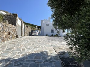 Calle adoquinada de piedra que lleva a un edificio blanco con un coche pequeño estacionado al frente.