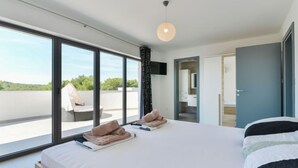 A modern bedroom with a large bed, a view of the outdoors, and a ceiling light. - Vacation home East by Interhome (Vodice/Tribunj)
