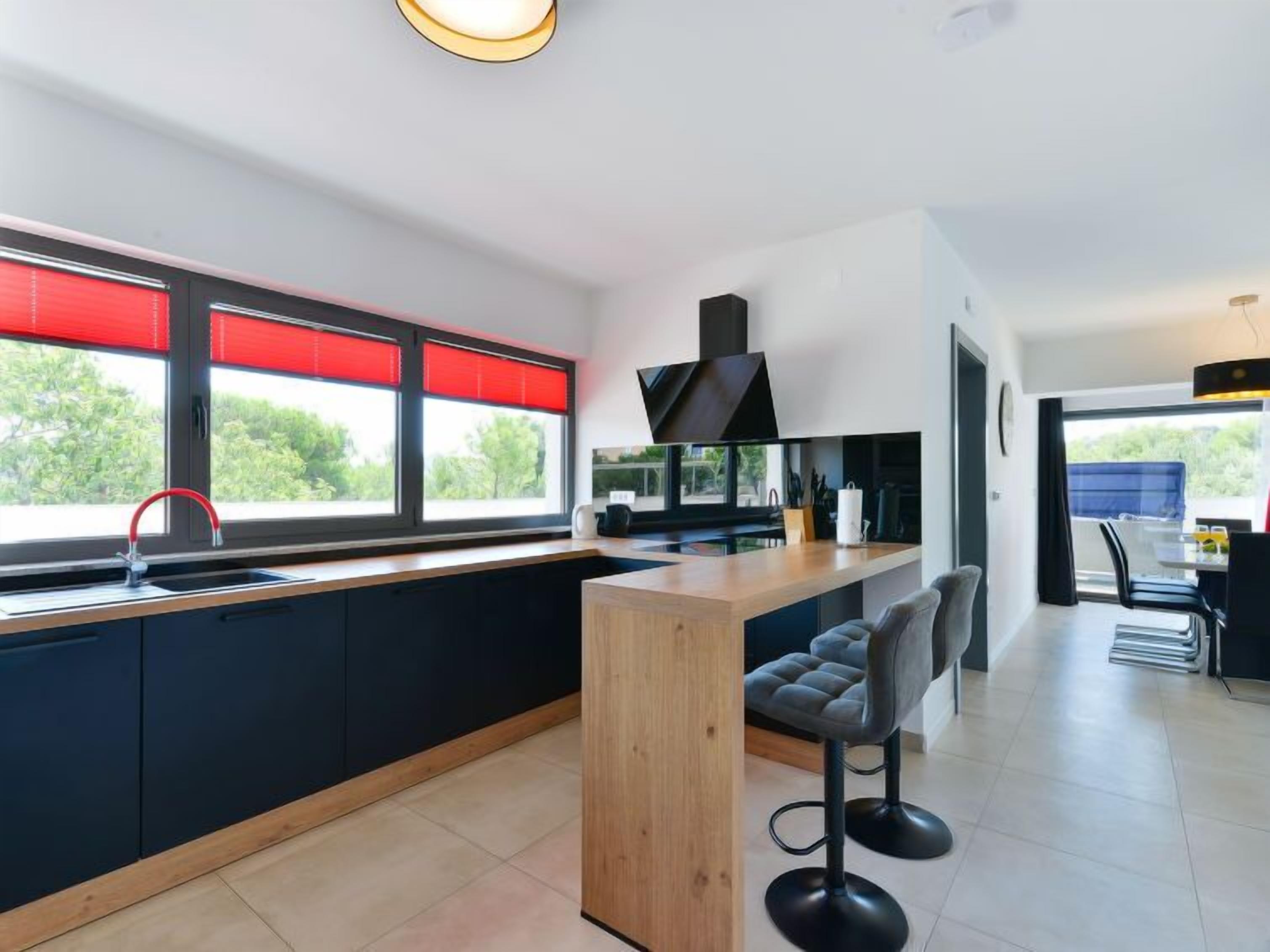 A modern kitchen with a central island, black cabinets, and a red faucet.