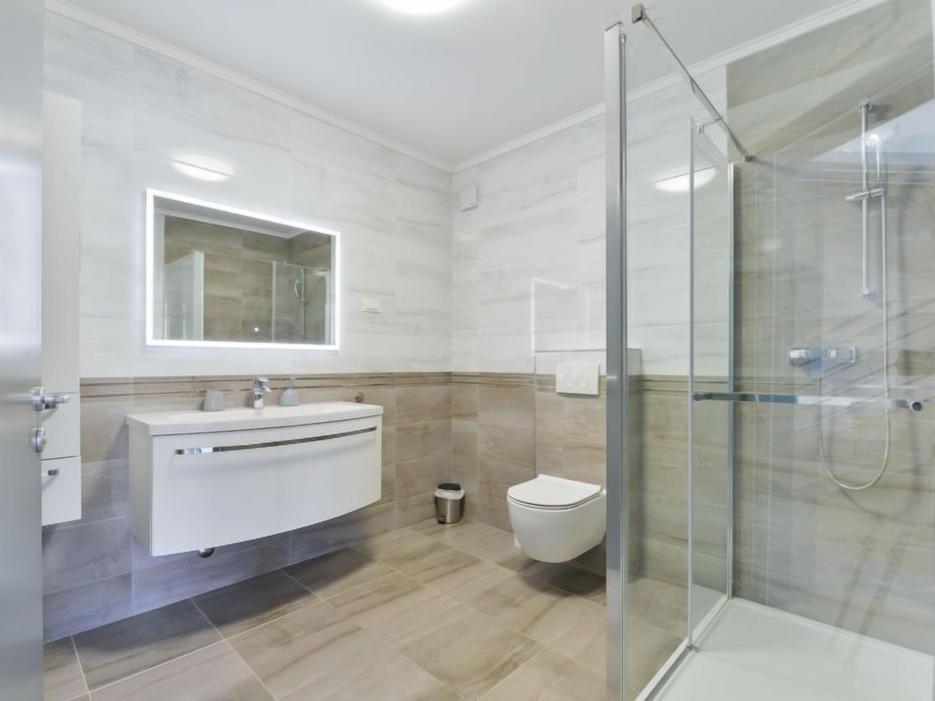 Een moderne badkamer met een glazen douchecabine, een witte wastafel met spiegel en een toilet.