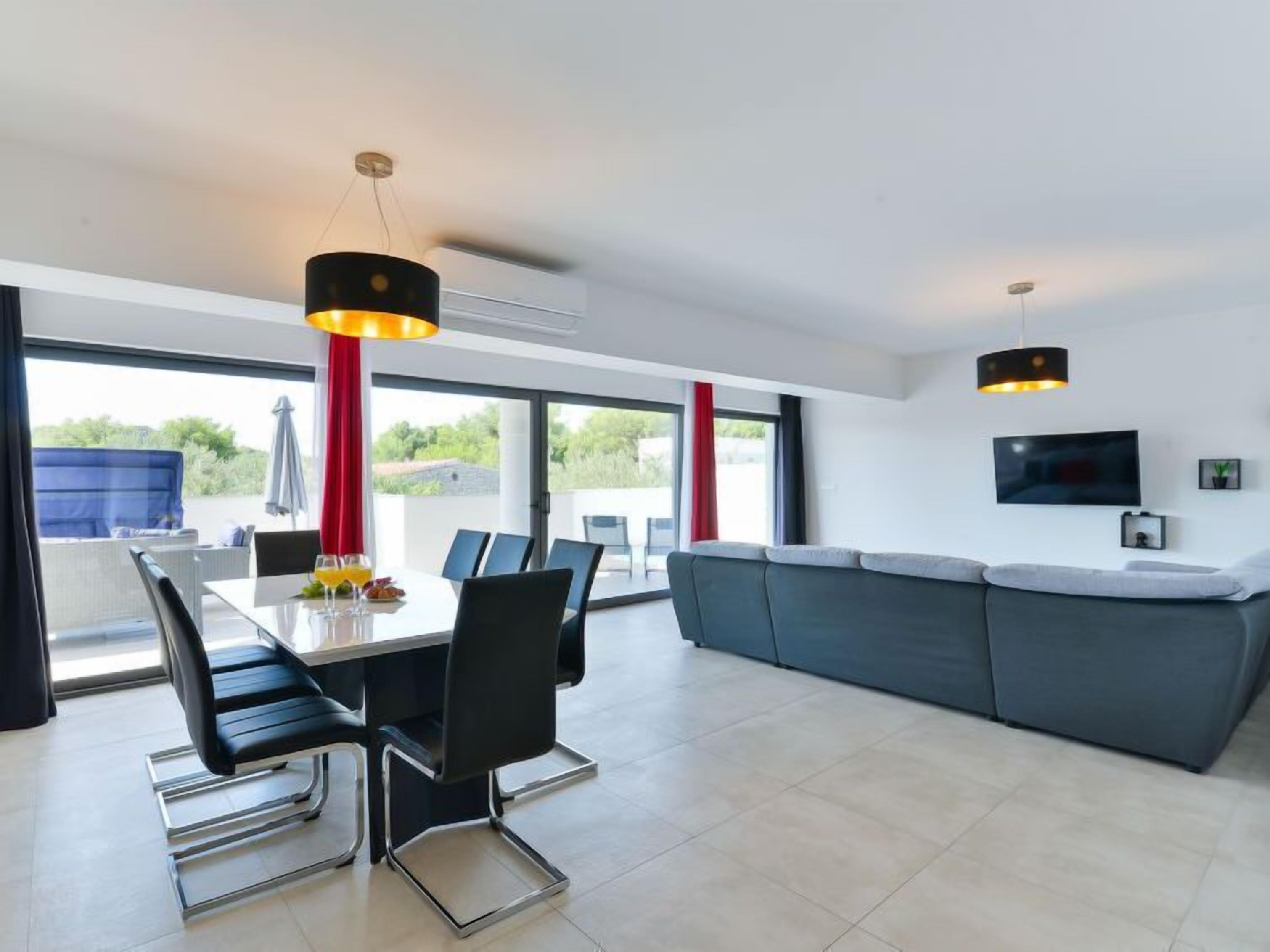 A modern living room with a dining area, large windows, and a flat-screen TV.