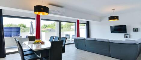 A modern living room with a dining area, large windows, and a flat-screen TV.
