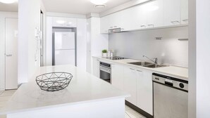 A modern kitchen with white cabinetry, a built-in dishwasher, and a stainless steel refrigerator. - Chevron Renaissance Ocean View (Surfers Paradise)