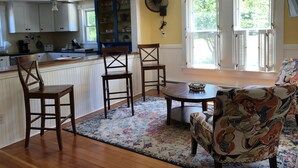 A kitchen with wooden cabinets, a dining area with a round table and chairs, and a window with shutters. - Only 2 Minutes Walk to Boardwalk, Beach, Eats & Fun! Large Well-Appointed Home. (Weirs Beach, Laconia)
