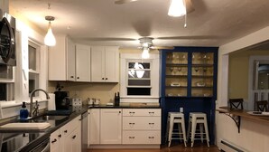 A kitchen with white cabinets, a black countertop, a window, and a blue wall with shelves. - Only 2 Minutes Walk to Boardwalk, Beach, Eats & Fun! Large Well-Appointed Home. (Weirs Beach, Laconia)