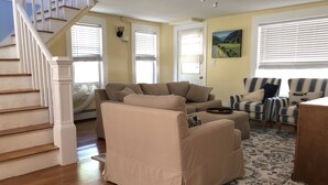 A living room with a beige sofa, striped armchairs, a wooden staircase, and a painting on the wall. - Only 2 Minutes Walk to Boardwalk, Beach, Eats & Fun! Large Well-Appointed Home. (Weirs Beach, Laconia)