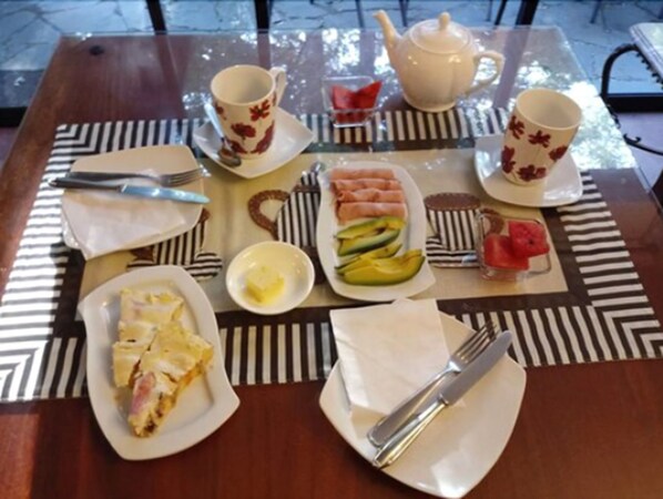 Un desayuno con tetera, tazas, platos de comida y cubiertos sobre una mesa con mantel individual a rayas.