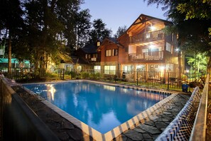 Un edificio de madera de dos pisos con piscina, borde de piedra y patio amurallado.