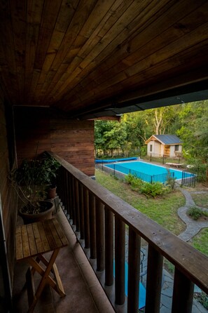 Ein hölzerner Balkon mit Blick auf einen Swimmingpool und ein kleines Haus im Hintergrund.