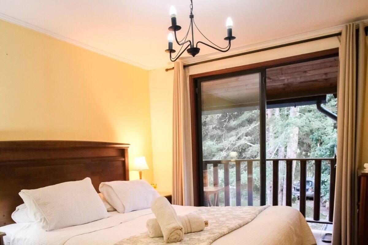 Una habitación de hotel con una cama grande, un candelabro, un balcón con vistas a árboles y un cabecero de madera.