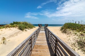 Une promenade en bois qui mène à la plage, avec du sable et des dunes de chaque côté.