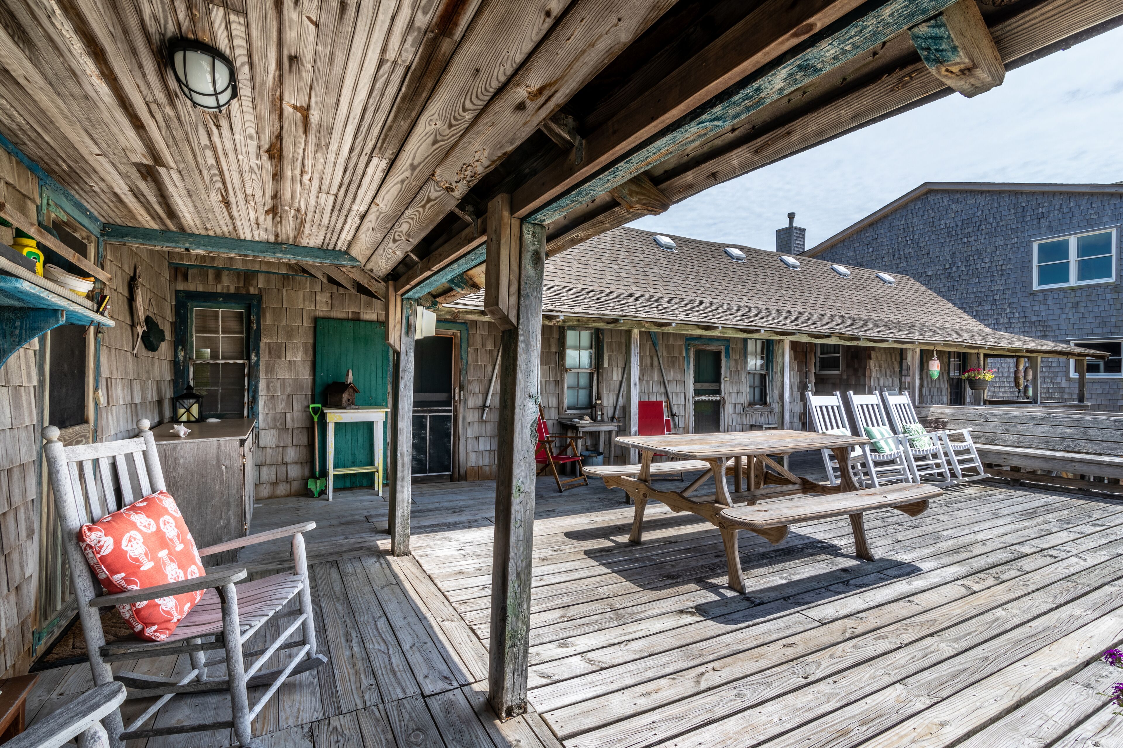Une terrasse en bois avec une table de pique-nique et des chaises, un fauteuil à bascule et une porte verte.