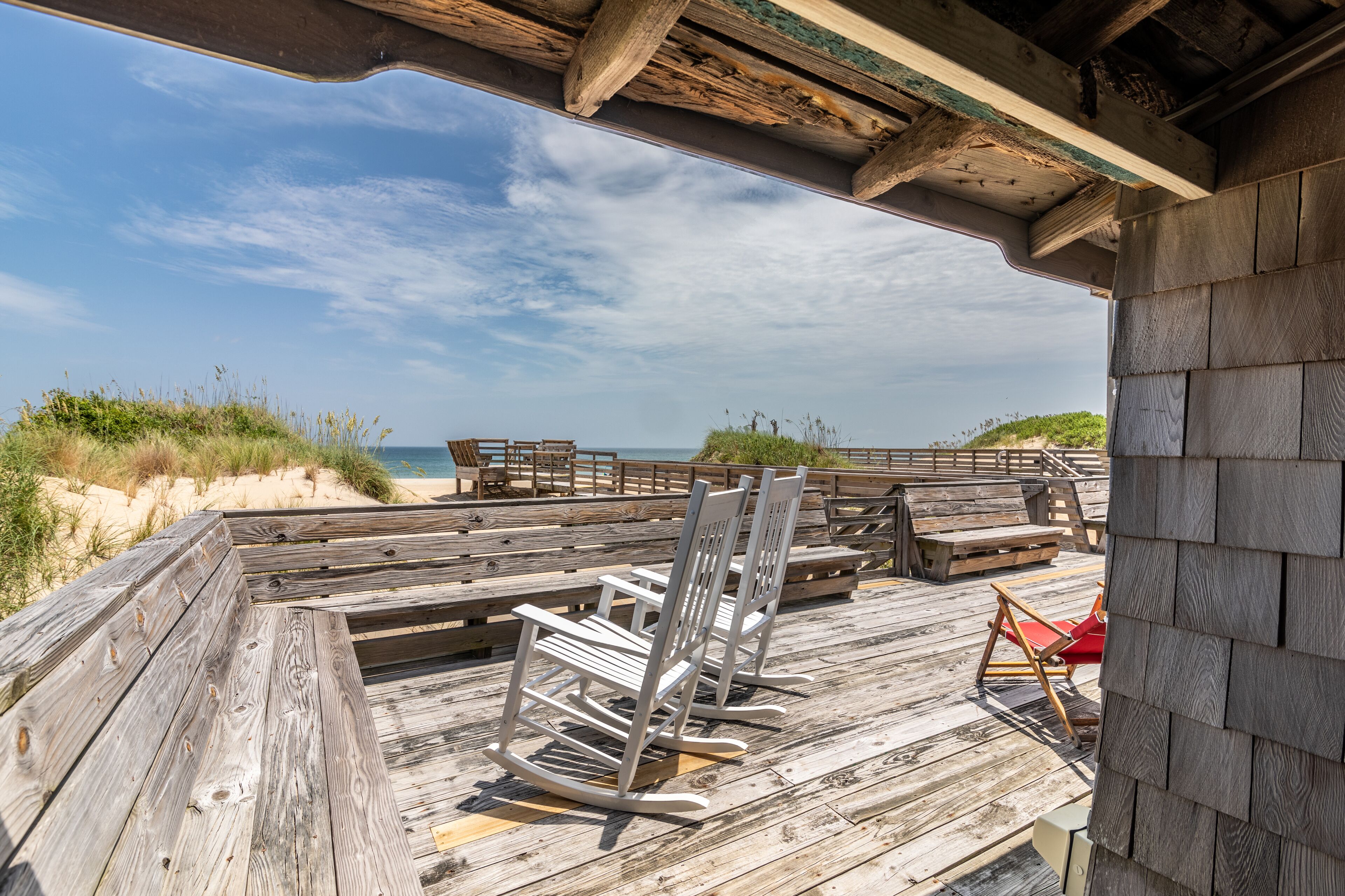 Eine Holzterrasse mit Bänken und einem Schaukelstuhl, mit Blick auf einen Strand.