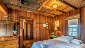 Een kamer met houten lambrisering, een bed, een dressoir, een deur en een raam.