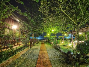 A nighttime garden pathway with a brick walkway, surrounded by lush greenery and illuminated by overhead lights. - WangWang B&B (Magong)
