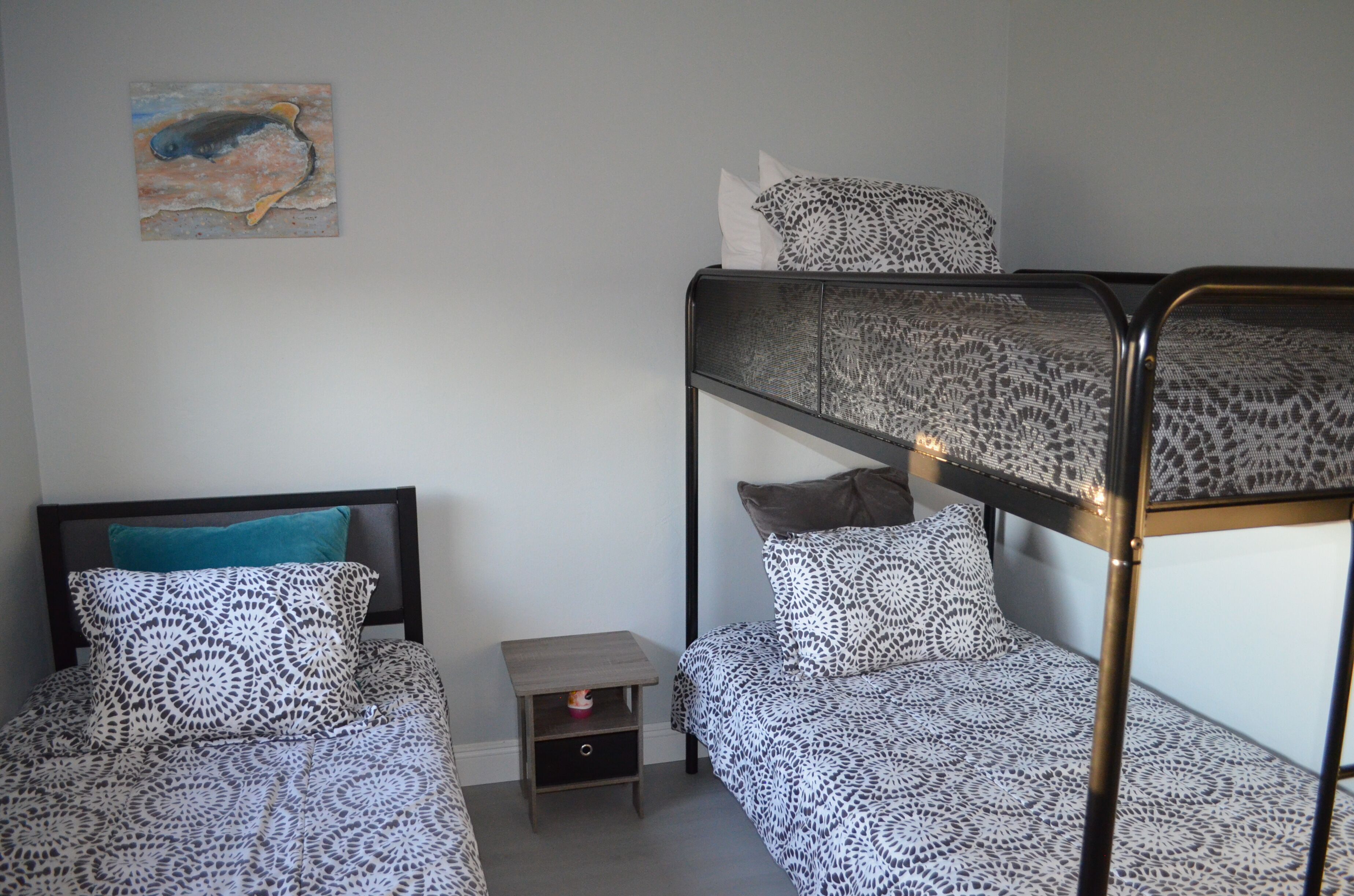 Une chambre avec un lit superposé, une literie à motifs, une petite table de chevet et une œuvre d’art murale.