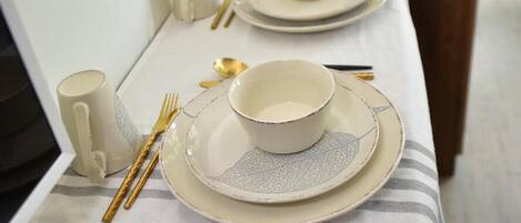 A neatly set dining table with plates, bowls, and cutlery, a kettle, and a roll of paper towels on a tablecloth.