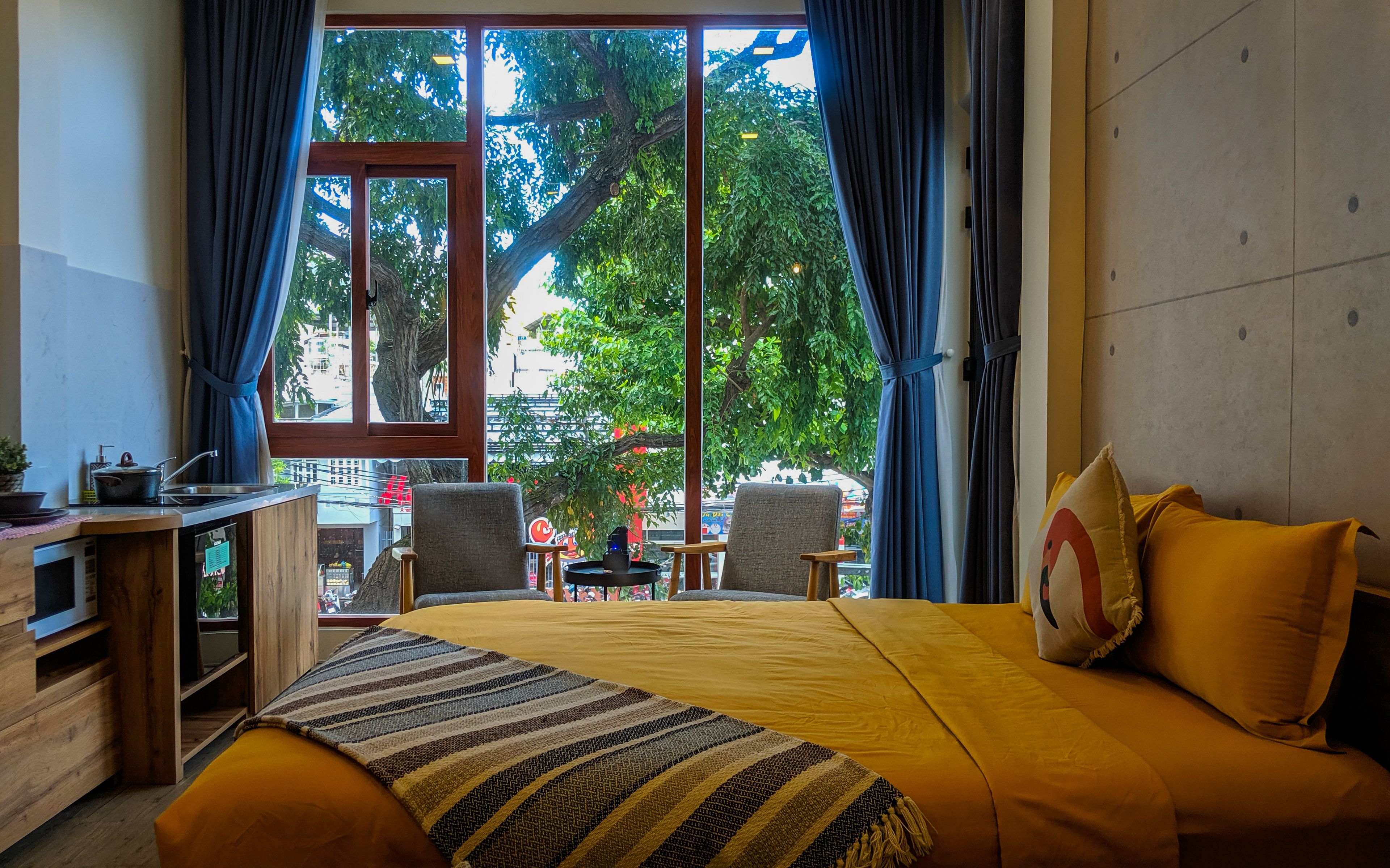 Ein Hotelzimmer mit einem großen Bett, einem Schreibtisch mit Stuhl, einem kleinen Tisch und Blick auf Bäume und Gebäude.