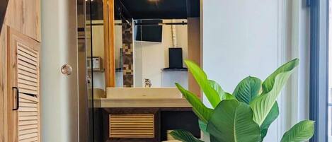 A modern bathroom with a wooden floor, a large potted plant, and a glass door leading to a shower area.