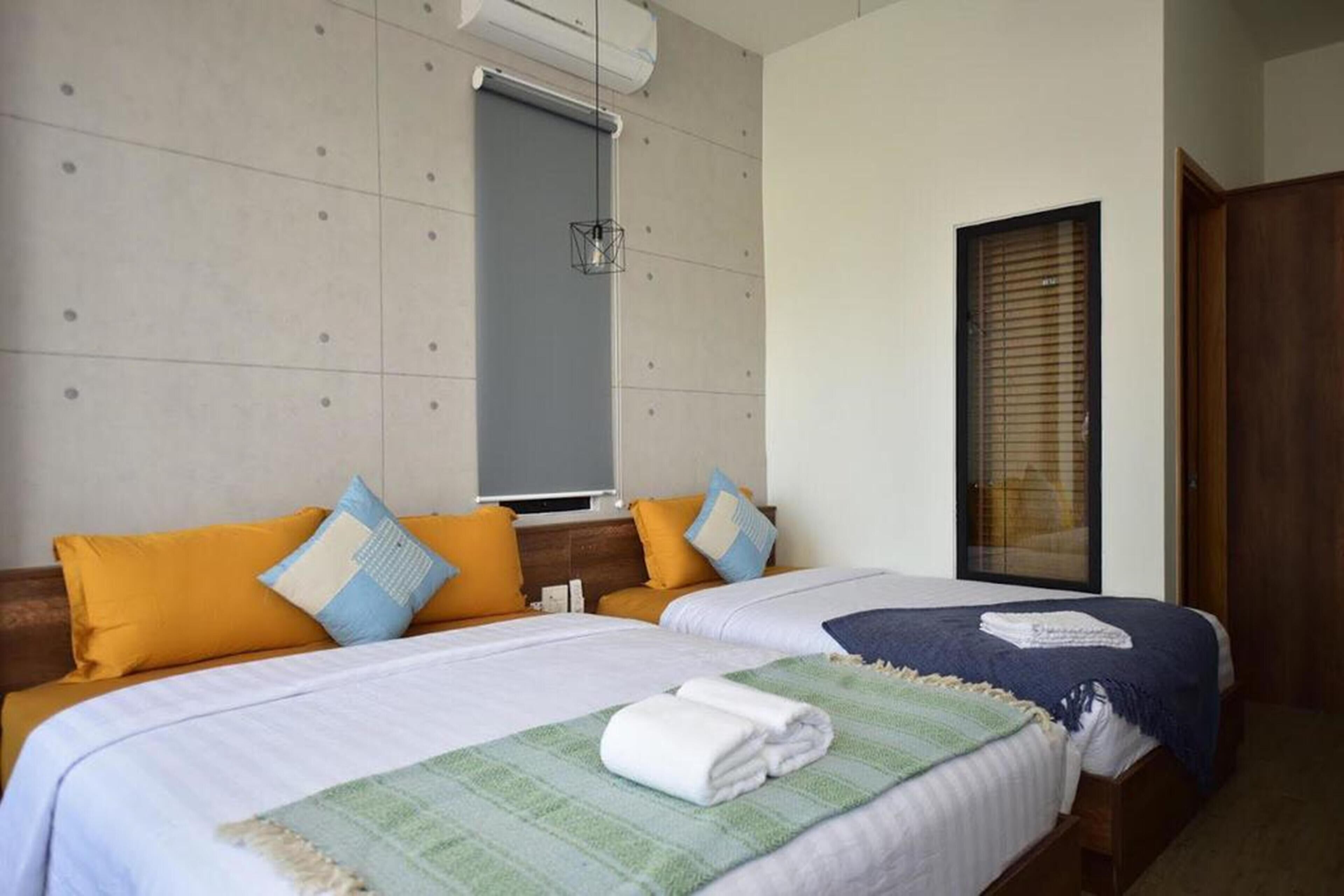 A hotel room with two beds, each with a different color blanket, a large mirror, and a window with blinds.