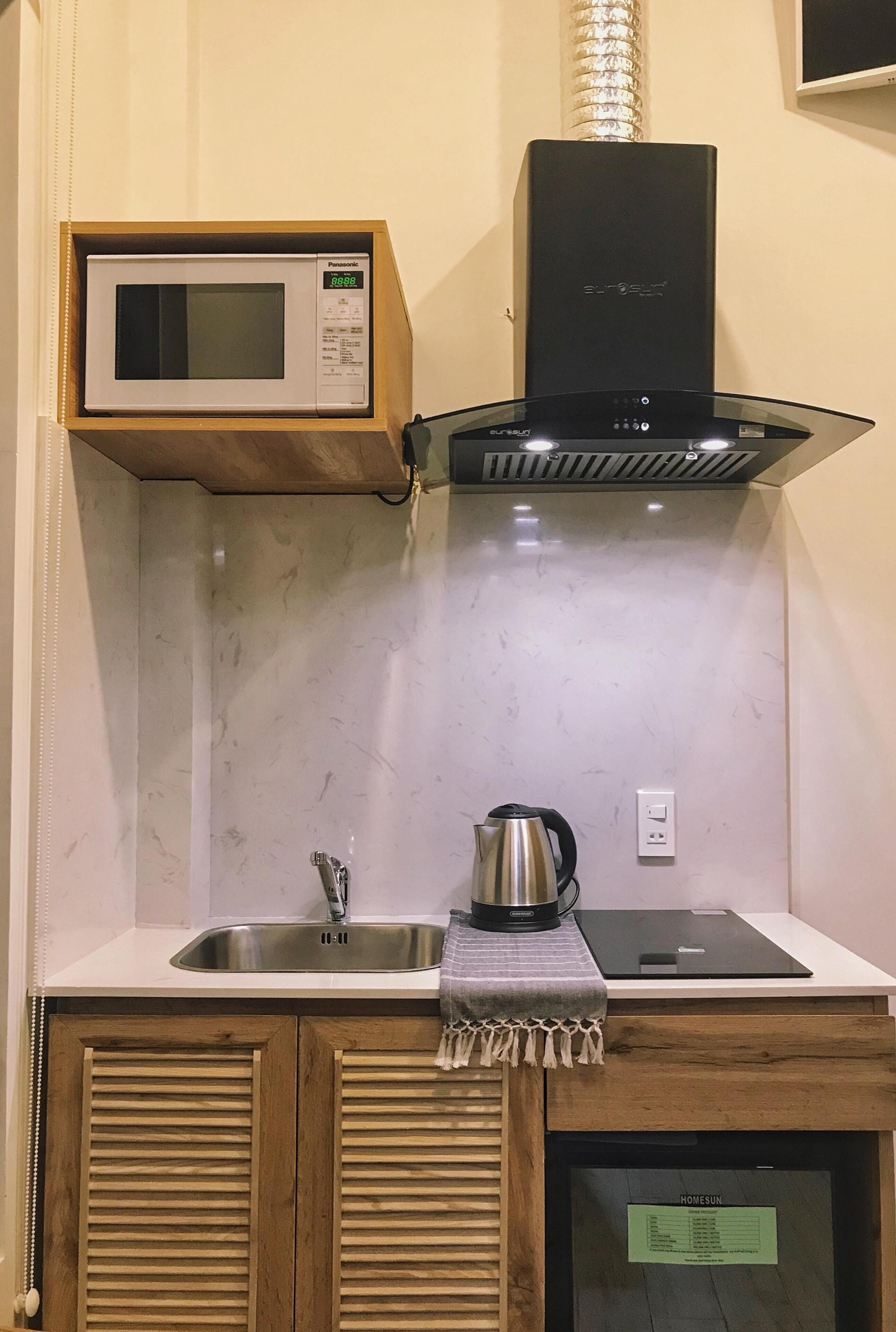 Une cuisine compacte équipée d’un four à micro-ondes, d’une hotte de cuisinière, d’un évier, d’une bouilloire et d’une tablette posée sur le plan de travail.