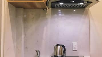 Une cuisine compacte équipée d’un four à micro-ondes, d’une hotte de cuisinière, d’un évier, d’une bouilloire et d’une tablette posée sur le plan de travail.