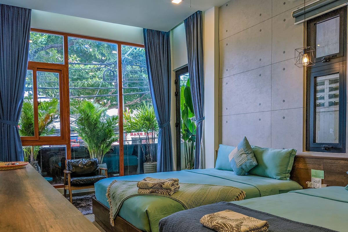 Habitación de hotel moderna con un ventanal grande, un escritorio de madera, dos camas y vistas a zonas verdes.