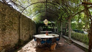 A stone-walled patio with a round table and chairs, a hanging light fixture, and a dog sitting at the table. - Luxury Suite in Renaissance Villa (Grassina)
