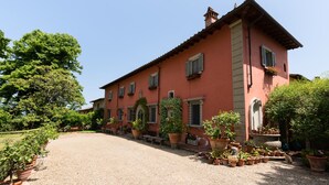 A large, single-story building with a red facade, multiple windows, and a gravel driveway. - Luxury Suite in Renaissance Villa (Grassina)