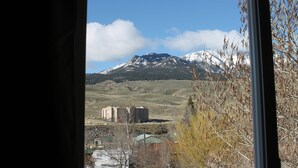 Vista attraverso una finestra su un paesaggio montuoso, con un edificio in primo piano.